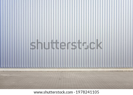 Exterior wall of warehouse made of aluminum sheet and paved road in outdoor area as background image. Texture of a wall made of silver corrugated metal sheet. 