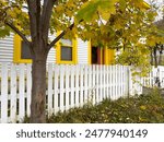 The exterior of a white cape cod clapboard horizontal wooden board style siding wall with two bright yellow trim windows. There