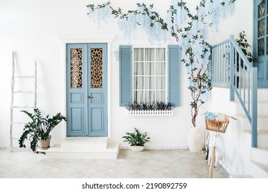 Exterior of a white mediterranean-style house with a blue door and a window, a flowering tree. Traditional patio of Santorini
