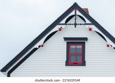 Exterior white wooden wall of horizontal clapboard siding on a vintage house with black trim. There's a small four pane glass window with red trim and a decorative gable roof. The background is white.