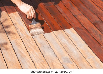 Exterior wood deck renovation, annual refreshing, worker's hand is oiling terrace decking with a painting brush after sanding