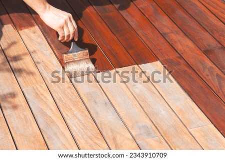 Exterior wood deck renovation, annual refreshing, worker's hand is oiling terrace decking with a painting brush after sanding