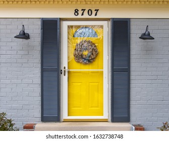 Exterior Yellow Front Door With Vintage Lights And Shutters With A Painted Grey Brick Background. 