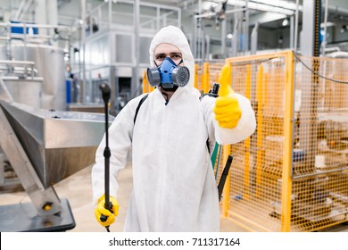 Exterminator in industrial plant spraying pesticide with sprayer.