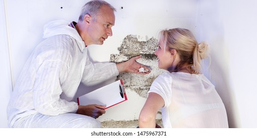 a exterminator or pest control contractor in work wear and grey hear squads with the female blonde customer at a mold destrtoyed wall and he explain the tasks to fight against the pests and mold