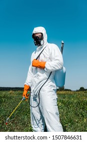 exterminator in white uniform and latex gloves holding spray against sky  