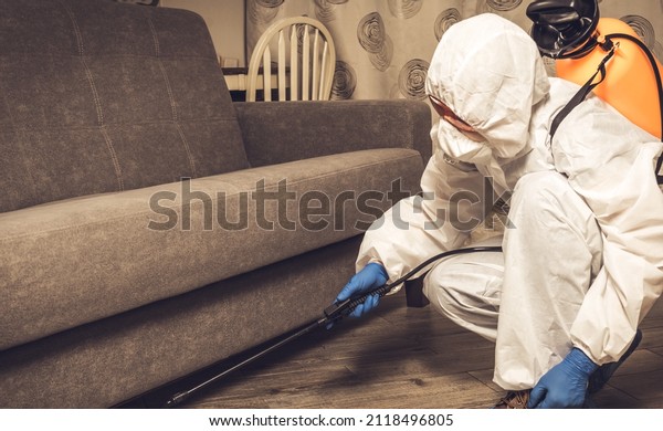 An exterminator in work clothes sprays\
pesticides with a spray gun. Fight against insects in apartments\
and houses. Disinsection of the\
premises.