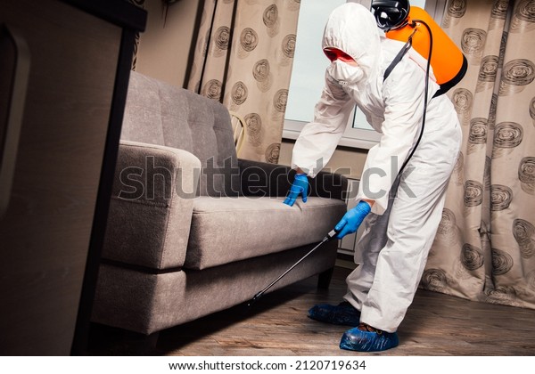 An exterminator in work clothes sprays\
pesticides with a spray gun. Fight against insects in apartments\
and houses. Disinsection of the\
premises