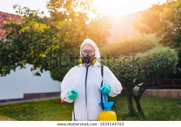 Exterminator in work wear outdoors spraying\
pesticide with\
sprayer