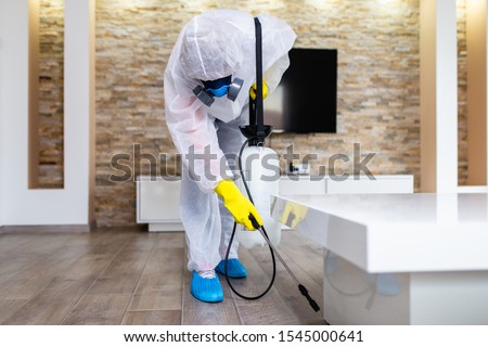 Exterminator in work wear spraying pesticide with sprayer. 