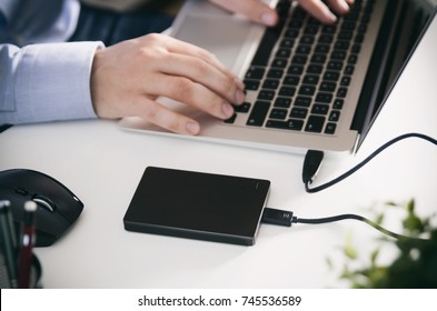 External Backup Disk Hard Drive Connected To Laptop. Man With Notebook Making Safety Personal Data Copy.