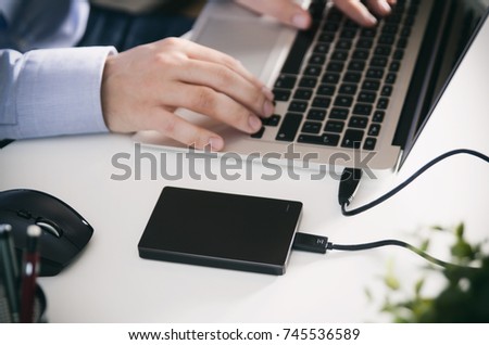 External backup disk hard drive connected to laptop. Man with notebook making safety personal data copy.