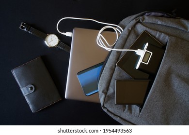 An external battery - power bank and many modern gadgets: smartphones, laptop and tablet are in a trendy gray city backpack. Charge your gadgets while traveling and trip. Black background. Close-up