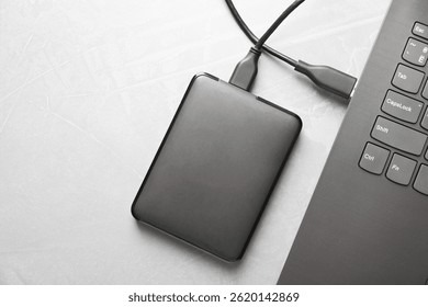 External hard disk connected to laptop on gray textured table, top view