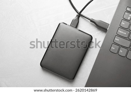 External hard disk connected to laptop on gray textured table, top view