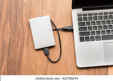 External hard drive connect to laptop computer on wooden background
