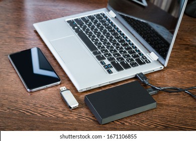 External hard drive connected to the laptop, USB flash drive and black smartphone on a brown wooden background. The concept of mobile technology