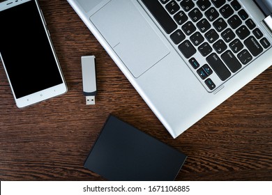 External hard drive connected to the laptop, USB flash drive and smartphone on a brown wooden background, flat lay. The concept of mobile technology