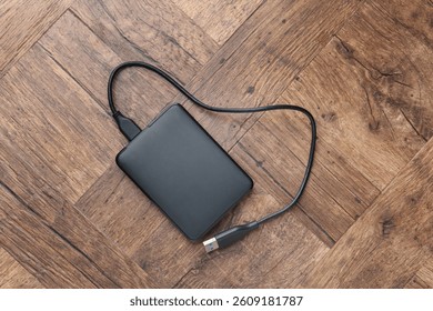 External hard drive with USB cable on wooden table, top view
