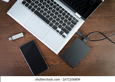 External hdd connected to the laptop, USB flash drive and smartphone on a brown table, top view. The concept of portable data storage