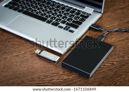 An external hdd connected to the laptop with a usb cable on a brown table. Portable storage technologies