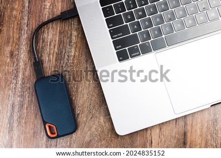 An external SSD Drive and a computer on wooden background. Selective focus.