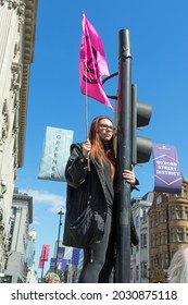 Extinction Rebellion Protestors At Oxford Circus Protesting About Climate Change. Girl Standing On The Traffic Lights Holding A Pink Flag. London - 25th August 2021