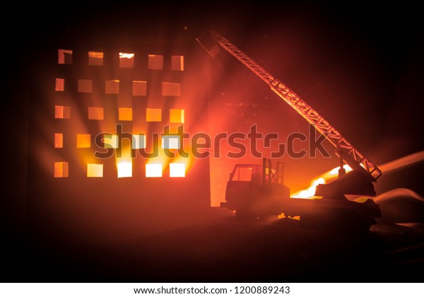 extinguish the fire of a private house at night.\
Toy fire truck with long ladder and burning building at night. Fire\
alarm concept. Selective\
focus