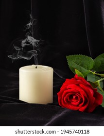 An extinguished candle and a red rose on a black background. The concept of mourning, condolences, funerals.