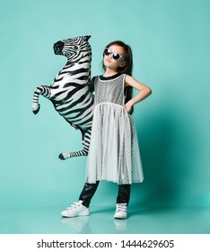 Extra Cool Asian Baby Girl Kid In High Fashion Luxury Dress And Sunglasses Poses With Zebra Metallic Balloon And Makes A Kissy Face On Blue Mint Background