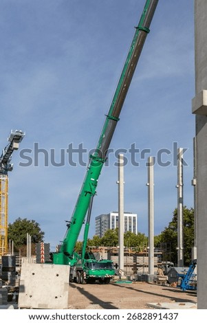 Extra heavy weight load mobile boom crane working modern city construction site with many concrete pillars blue sky background. Telescopic boom lifting equipment rental service. Industrial machinery