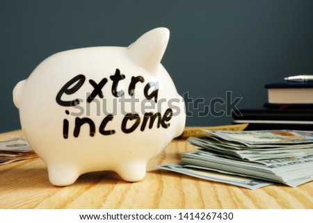 Extra income handwritten on a piggy bank and cash.