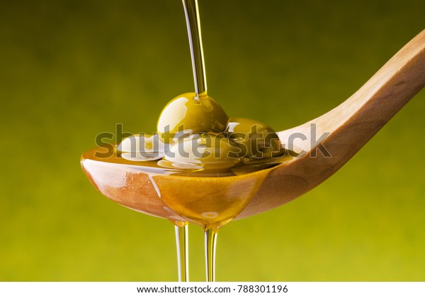 extra virgin olive oil flows on a wooden bowl full\
of green olives
