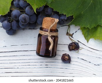 Extract, Oil In A Bottle, Ripe Blue Grapes With Green Leaves On A White Wooden Table, Flat Layout. Cosmetic Product With Harvest Fruit Plant Vitis