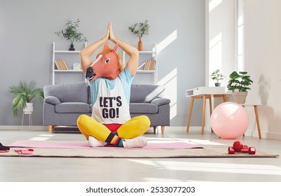 Extraordinary approach to yoga. Man in horse mask is doing funny yoga and performing asana in cozy home interior. Eccentric man sits in lotus position on yoga mat with horse mask on his head. - Powered by Shutterstock