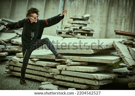 An extraordinary mature man with dreadlocks and tattoos in black clothes with ethnic ornaments poses expressively on the backstreet. Rock and punk culture. Copy space.