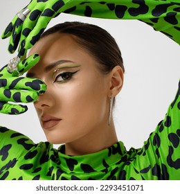 Extravagant eye makeup with bright green arrows, stylish young woman in a green leopard bodysuit, studio portrait close-up