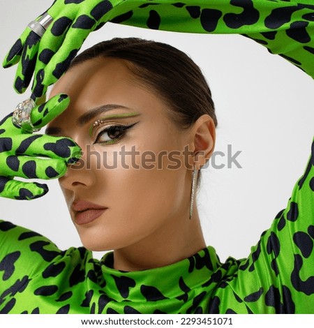 Extravagant eye makeup with bright green arrows, stylish young woman in a green leopard bodysuit, studio portrait close-up