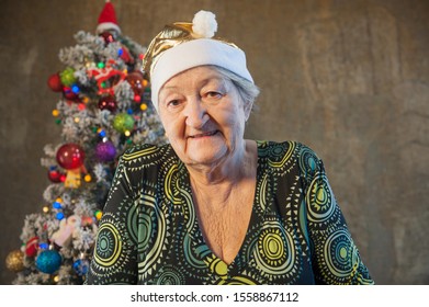 Extravagant Old Woman With Gray Hair And Wrinkles In Glasses. Senior Citizen In Santa Claus Hat. Concept Of Domineering And Funny Elderly Mother In Law. Christmas Eve