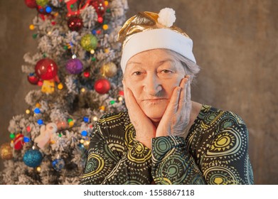 Extravagant Old Woman With Gray Hair And Wrinkles In Glasses. Senior Citizen In Santa Claus Hat. Concept Of Domineering And Funny Elderly Mother In Law. Christmas Eve