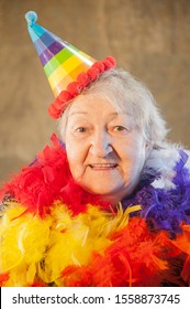 Extravagant Old Woman With Gray Hair And Wrinkles In Glasses. Senior Citizen In Carnival Hat And Colored Feathers Around Neck. Concept Of Domineering And Funny Elderly Mother In Law. Christmas Eve