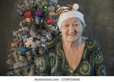 Extravagant Old Woman With Gray Hair And Wrinkles In Glasses. Senior Citizen In Santa Claus Hat. Concept Of Domineering And Funny Elderly Mother In Law. Christmas Eve