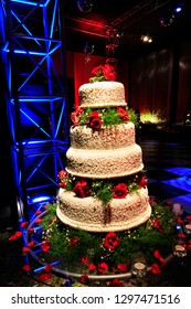 Extravagant Round Wedding Cake With Decorative Icing And Red Roses Set Against Blue Ambient Lighting.