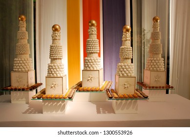 Extravagant Wedding Desserts Table With Five Elaborately Decorated Cake Holders Set Against A Multi Coloured Fabric Background.