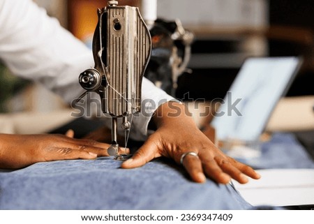 Extreme close up of african american seamstress using industrial sewing machine on fabric material in atelier shop workstudio. Dressmaker cutting clothing garment piece, manufacturing bespoke outfits