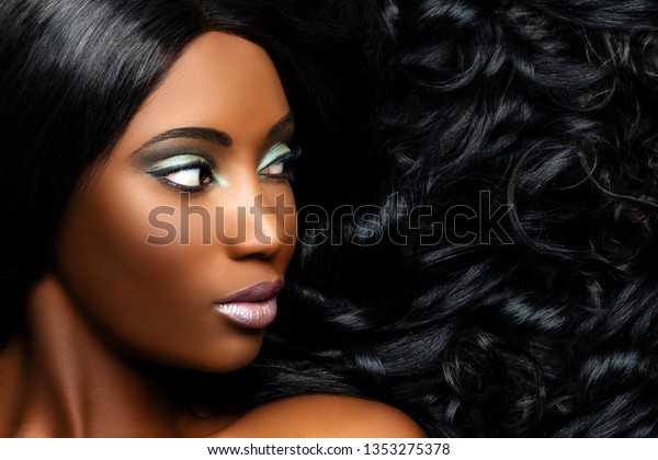 Extreme close up beauty portrait of beautiful\
young african woman with professional make up. Girl looking aside\
with long curly hair next to\
face.
