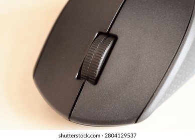 Extreme close up of a black wireless computer mouse scroll wheel and textured surface