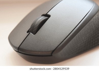 Extreme close up of a black wireless computer mouse scroll wheel and textured surface