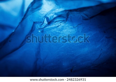 Extreme close up of blue empty plastic bag background. The plastic surface is wrinkly and tattered making abstract pattern. Selective focus, shallow depth of field.