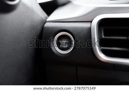 Extreme close up of car engine start stop button on dashboard. Modern vehicle ignition system button with chrome ring. Automobile dashboard interior detail, keyless technology and part concept